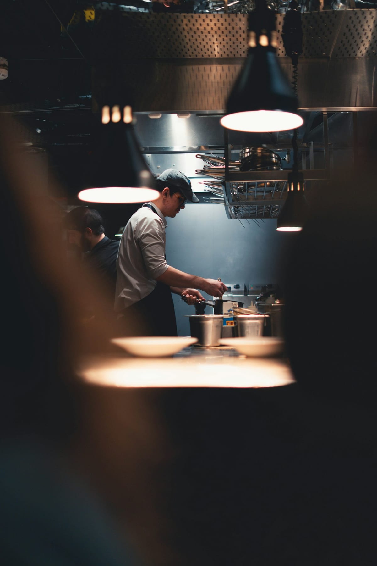 A chef cooking under the pass lamps in a professional kitchen during evening service
