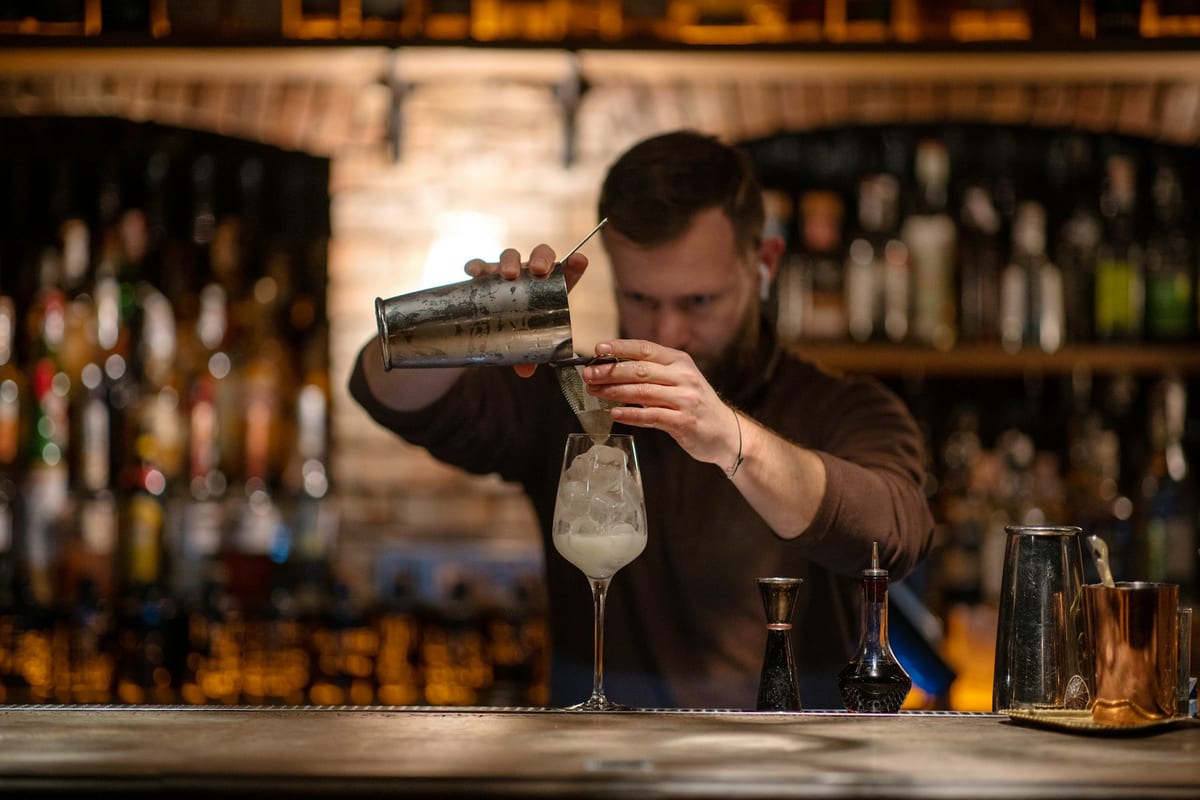 A bartender finishing a cocktail at a dimly lit bar during evening service