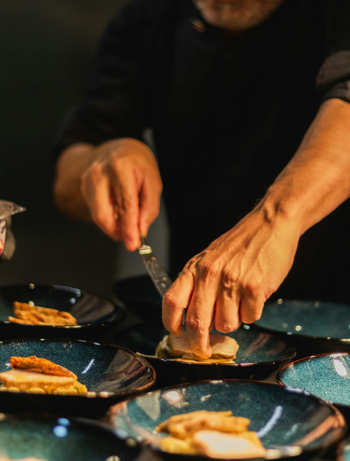 A chef's hands plating a dish during service — where most hospitality training actually happens