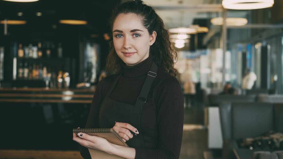 A restaurant manager in an apron holding a notepad in a quiet bar